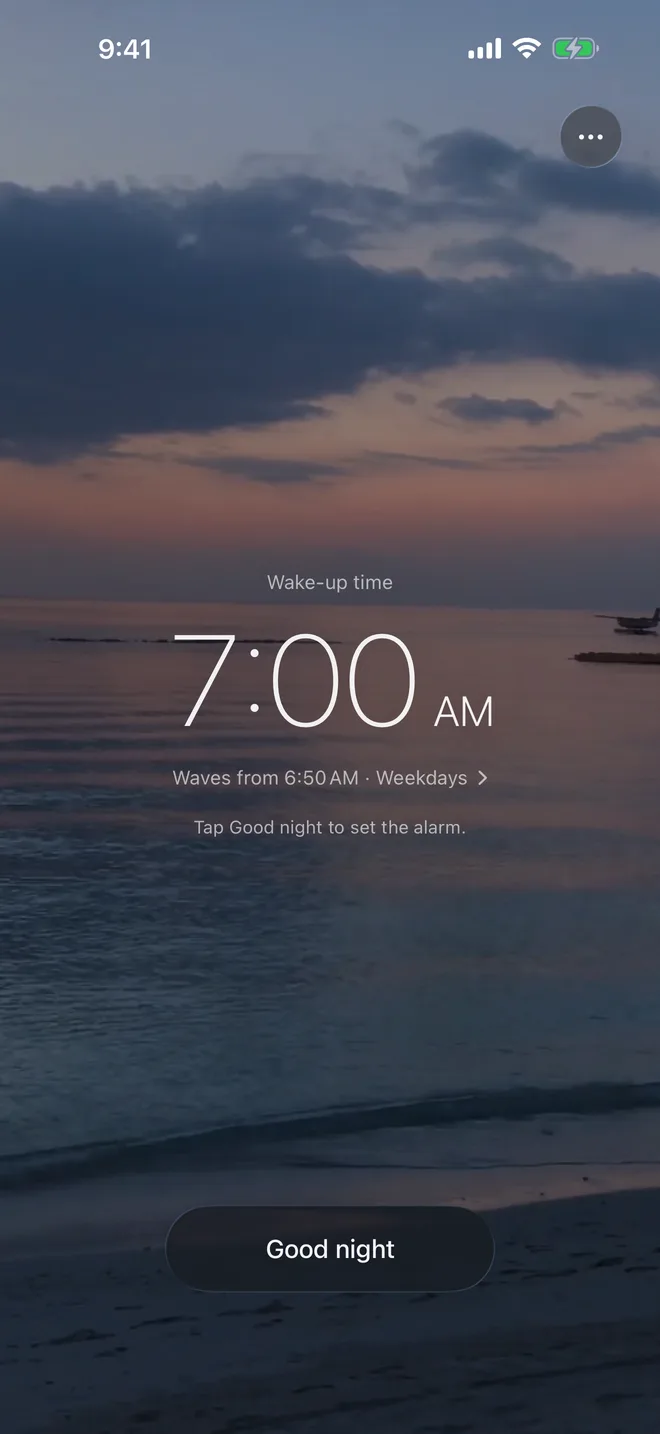 The first screen of Petit Ocean on an iPhone: a beach at dusk, the wake-up time 7:00 AM in large thin numbers, waves from 6:50 AM on weekdays, and a Good night button.